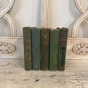 May include: A collection of five vintage hardcover books with green and brown spines. The titles include The Quest of the Golden Girl, The Right of Way, and Tried for Her Life. The books feature decorative gold and black lettering and patterns.