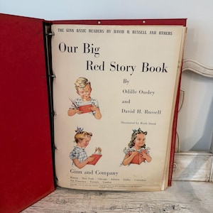 May include: A vintage red binder containing the book titled Our Big Red Story Book by David H. Russell and others, illustrated by Ruth Steed. The cover features black text and three color illustrations of children reading books.