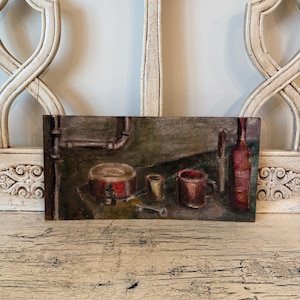 May include: An oil painting depicts a still life with a red bottle, a mug, a small cup, and a round container. The painting has a muted color palette with brown, red, and green tones. A knife and a wrench are also visible.