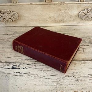 May include: A vintage book with a deep red cover, titled "Toy Making" and "Hawthorne" visible on the spine. The book is resting on a distressed, white-painted wooden surface, suggesting an antique or collectible item.