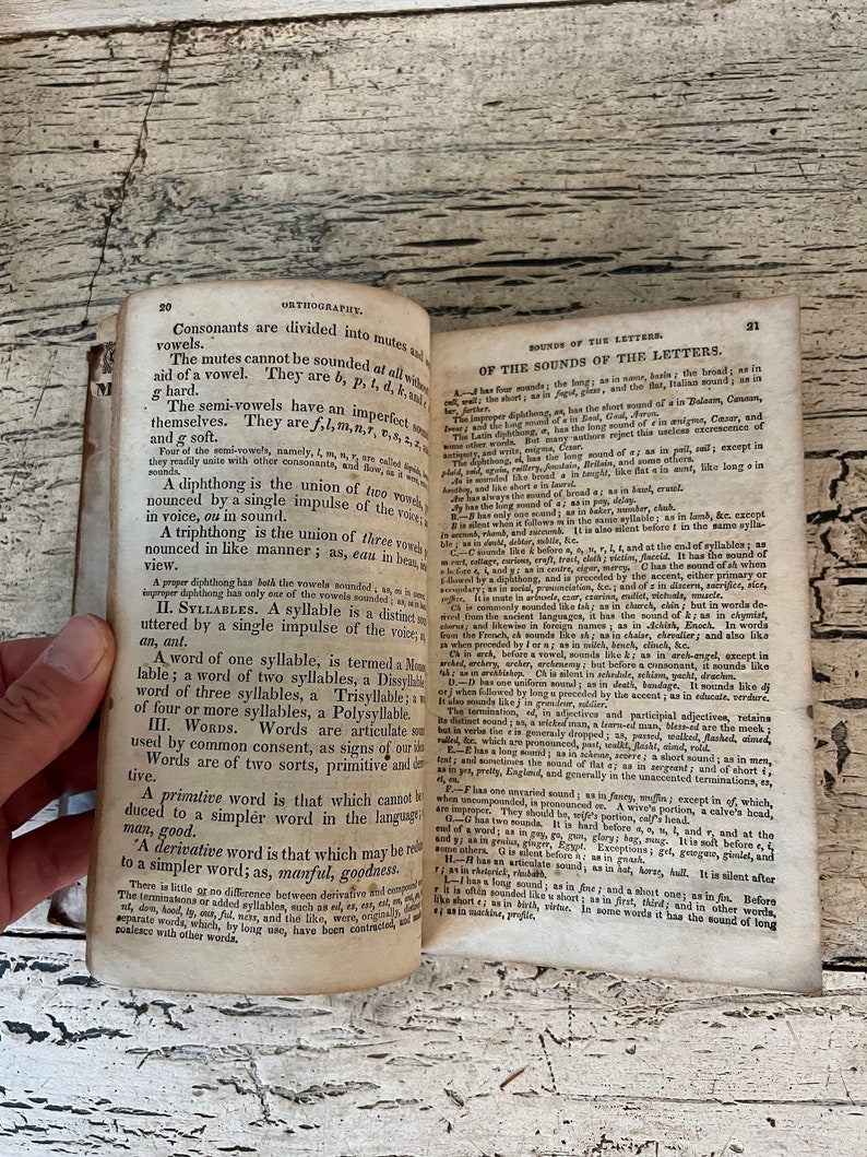 May include: A page from an old book about the sounds of letters in the English language. The page is yellowed and has a worn, aged appearance. The text is in black ink and discusses the sounds of consonants and vowels, diphthongs, triphthongs, and syllables.