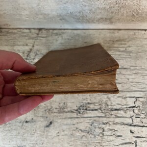 May include: A brown leather-bound book with aged pages. The book is closed and the spine is visible.