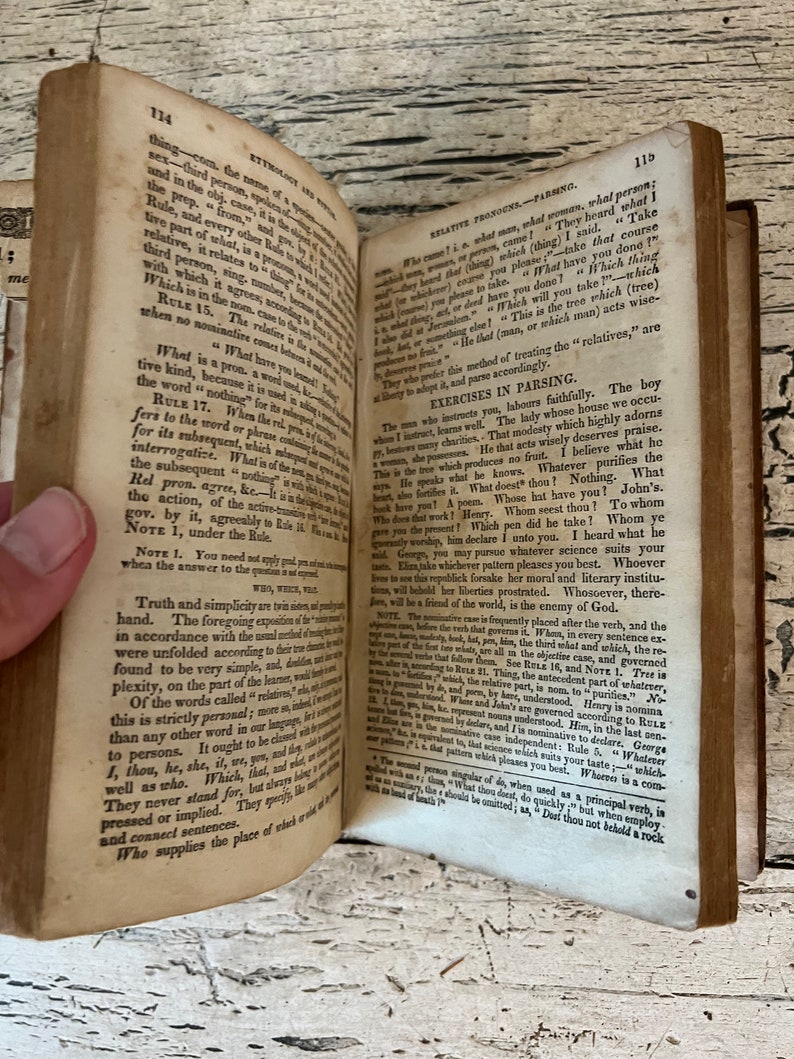 May include: An open book with yellowed pages and a brown leather cover. The book is open to a page with text about grammar and the use of relative pronouns. The text is in a small font and is difficult to read.