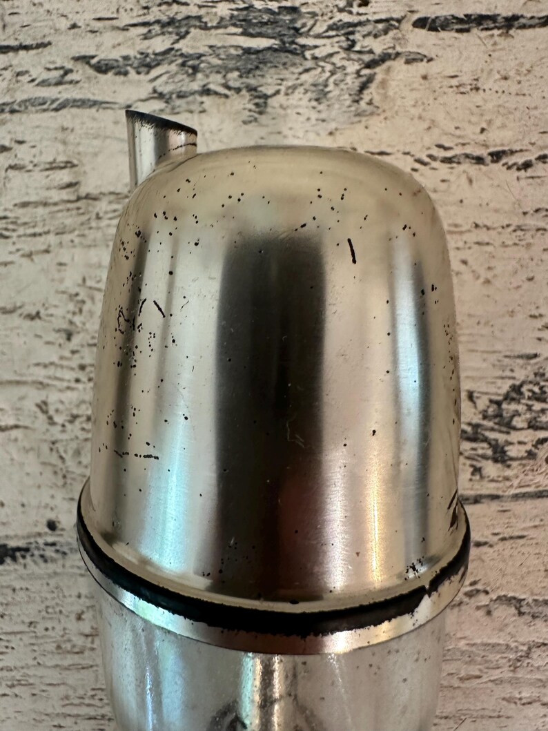May include: A silver metal bottle stopper with a spout. The stopper has a black rubber seal around the top.
