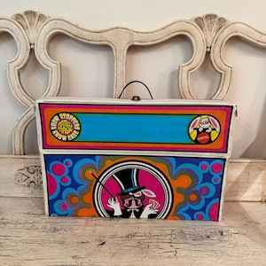 May include: A rectangular Mattel Magic Show Case with a handle and a colorful graphic design. The front features a rabbit in a top hat holding playing cards, surrounded by blue, orange, and pink patterns, with the text Show Stoppers Mattel Magic.