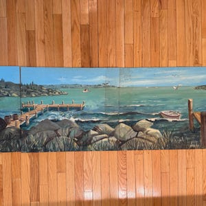 May include: A four-panel panoramic painting depicting a coastal harbor scene with red wooden buildings, a wooden pier, rocky shoreline, and a small boat on the water. The artwork features a blue sky, green sea, and natural landscape elements.