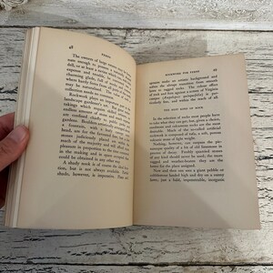 May include: Open book with pages displaying text about ferns and rockwork. The book is held open by a hand, revealing the text and the aged paper. The pages are yellowed with age, and the book is open on a wooden surface.