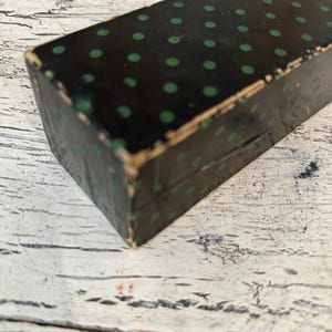 May include: A black box with a green polka dot pattern. The box is made of cardboard and has a worn, vintage look.