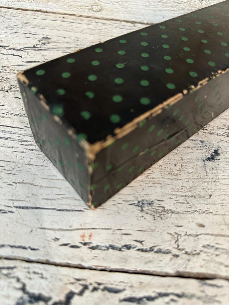 May include: A black box with a green polka dot pattern. The box is made of cardboard and has a worn, vintage look.
