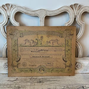 May include: An aged, rectangular document with ornate green and gold borders and illustrations. The document features text, seals, and a central illustration of a figure with a trident. The document is set against a white, ornate headboard.