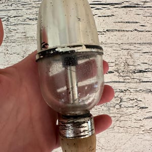 May include: A vintage silver and glass bottle stopper with a wooden handle. The stopper has a clear glass bulb with a metal insert and a silver top.