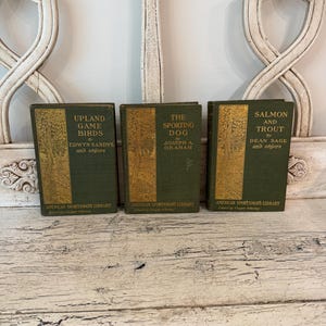 May include: Three hardcover books from the American Sportsman's Library with dark green covers and gold-toned decorative panels. The titles are Upland Game Birds, The Sporting Dog, and Salmon and Trout, each featuring author names and text.
