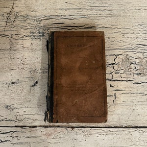 May include: A vintage brown book with the title "Arithmetic for Academies and Schools" on the cover.
