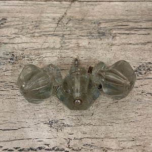 May include: Three clear glass cabinet knobs with a silver finish. The knobs have a faceted design.