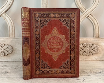 Op de afbeelding: Een rood lederen gebonden boek met gouden accenten en ingewikkelde ontwerpen. De titel op de omslag luidt "The Poems of Oliver Goldsmith, Illustrated".
