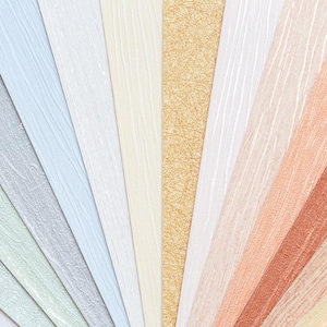 May include: A fan of textured wallpaper samples in various colors. The samples include shades of gray, blue, beige, gold, peach, and brown. The paper has a subtle, patterned design.
