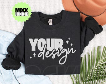 May include: Black crewneck sweatshirt with the words "YOUR design" in white script. The sweatshirt has a simple, classic design, perfect for customization. The image also includes a brown hat and a palm leaf.
