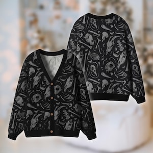 Könnte beinhalten: Schwarzes Cardigan- und Rundhals-Pullover-Set mit einem sich wiederholenden Muster aus grauen Tierschädeln und Knochen. Der Cardigan hat einen V-Ausschnitt, lange Ärmel und Holzknöpfe. Der Pullover hat einen Rundhalsausschnitt und lange Ärmel. Das Set ist aus weichem Material.