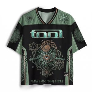 Può includere: Maglia nera e verde a maniche corte con scollo a V. La maglia presenta il nome della band "TOOL" in verde acqua, insieme a disegni geometrici e a forma di occhio. Il testo "TRANSCENDANCE THROUGH GEOMETRY" è stampato verticalmente.