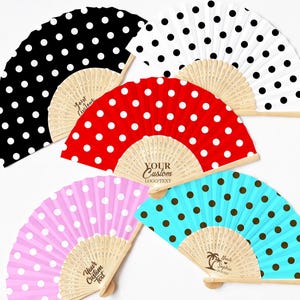 May include: Five folding hand fans with wooden ribs and fabric covers featuring polka dot patterns in black, white, red, pink, and light blue. The wooden ribs are engraved with text including "Your Custom", "Logo/Text", and "Noah & Sophia".