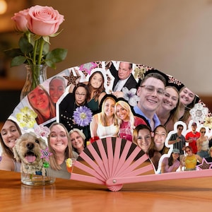 Peut inclure: Un éventail pliable semi-circulaire présentant un collage de diverses photographies personnelles de personnes et d'un chien, agrémenté de petits graphismes en forme d'étoiles et de fleurs. L'éventail possède une monture en plastique rose clair.