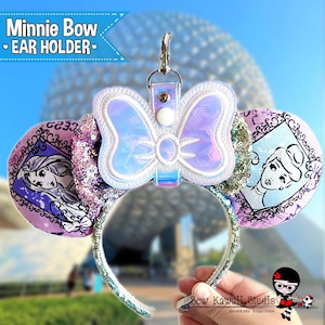 May include: A Minnie Bow ear holder with a holographic bow and a silver clip. The headband features images of Disney princesses and is decorated with sequins. The text "Minnie Bow Ear Holder" is visible in the upper left corner.