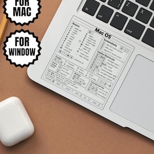 Puede incluir: Una pegatina rectangular blanca aplicada en el reposamuñecas de un portátil plateado, con una guía de referencia impresa en negro de atajos de teclado para Mac OS, incluyendo secciones de conceptos básicos, capturas y comandos.