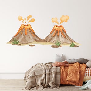 Puede incluir: Un adhesivo de pared con dos volcanes de dibujos animados en erupción con lava y humo naranja. Los volcanes son marrones y beige, con hierba verde y una base arenosa. La pegatina está en una pared blanca sobre una cama con ropa de cama naranja.