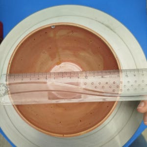 Puede incluir: Un cuenco de cer&aacute;mica hecho a mano con interior marr&oacute;n rojizo y borde marr&oacute;n claro. Una regla transparente se coloca sobre el cuenco, midiendo aproximadamente 15 cm de di&aacute;metro. El cuenco est&aacute; sobre una superficie gris y azul.