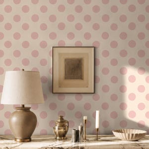 Può includere: Una credenza in legno scuro con piano in marmo presenta una lampada da tavolo con paralume beige, un piccolo barattolo in metallo con coperchio, due sottili portacandele in metallo e una ciotola poco profonda. La parete ha carta da parati a pois rosa.