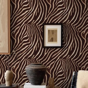 May include: A room interior featuring wallpaper with a dark brown and cream zebra stripe pattern. A wooden console table holds a dark ceramic vessel, stacked books, and a small sculpture. A black-framed artwork hangs on the patterned wall.