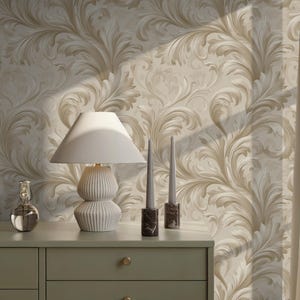 Könnte beinhalten: Eine Kommode in Salbeigrün mit goldenen Knöpfen, eine weiße Lampe und zwei Kerzen. Der Hintergrund ist eine cremefarbene Tapete mit einem wirbelnden Blumenmuster. Eine klare Glasflasche mit einem Verschluss befindet sich ebenfalls auf der Kommode.