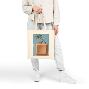 Può includere: Una borsa tote in tela beige con una stampa grafica di un grande tasto escape del computer color sabbia. Sopra il tasto si trovano una piccola palma e una persona che si rilassa su una sedia a sdraio contro un cielo azzurro con nuvole.