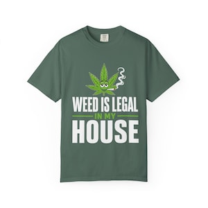 May include: Green t-shirt with the text "WEED IS LEGAL IN MY HOUSE". The shirt features a cartoon cannabis leaf with eyes and a lit cigarette. The design is in white and green.