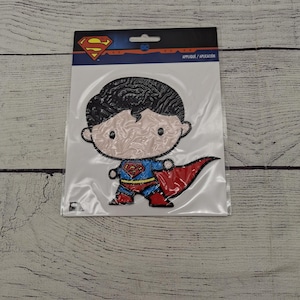 May include: Superman applique patch featuring a cartoon version of the superhero. The patch has a red cape, blue and red suit, and the Superman logo. The patch is on a white background with a DC logo.
