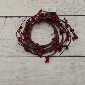 May include: A circular wreath made of brown twigs and adorned with bright red berries. The wreath is arranged in a circular shape, with the berries evenly spaced around the twigs. The berries are a vibrant red color, and the twigs are a natural brown.