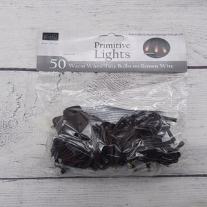 May include: A package of 50 warm white tiny bulbs on brown wire primitive lights. The package is labeled "Primitive Lights" and "50 Warm White Tiny Bulbs on Brown Wire".