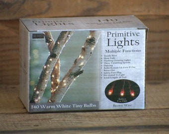 May include: A box of 140 warm white tiny LED lights on brown wire. The box shows a close-up of the lights wrapped around birch branches. The box also lists multiple functions for the lights, including steady burn, slow fade, flashing, and dancing.