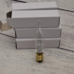 May include: Four clear glass candle-shaped light bulbs with a standard screw base. The bulbs are packaged in white cardboard boxes.