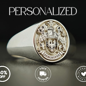 May include: A silver signet ring with a detailed crest engraving. The ring features the word "PERSONALIZED" above it. The crest includes an eagle and the name "BERGHOFER". The ring is on a dark background.