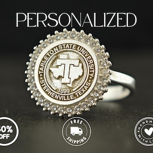 May include: A silver ring featuring the Tarleton State University emblem, encircled by sparkling clear stones. The ring's face displays the university's logo and the text "Stephenville, Texas 1899". The word "PERSONALIZED" is above the ring.
