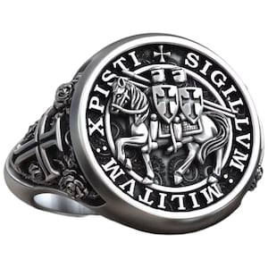 Könnte beinhalten: Silberfarbener Ring mit detailliertem Design eines Ritters zu Pferd, einem Kreuz und der lateinischen Inschrift "SIGILLVM MILITVM XPISTI". Der Ring hat eine runde Oberfläche und verzierte Details am Band mit floralem Muster.