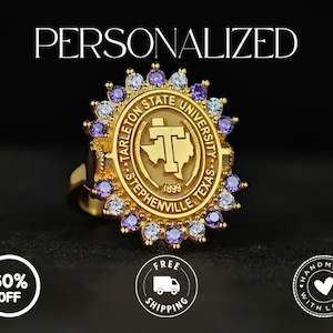 May include: A gold-colored ring featuring the Tarleton State University emblem, surrounded by purple and clear gemstones. The word "PERSONALIZED" is at the top. The ring has a detailed design and is set against a dark background.