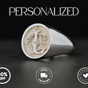 Op de afbeelding: Een zilveren zegelring met een gepersonaliseerd ontwerp. De ring heeft een cirkelvormige voorkant met een gegraveerd monogram en het woord "GEPERSONALISEERD" erboven. De ring ligt op een donkere ondergrond.