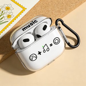 Può includere: Custodia bianca per AirPods con la scritta "music" stampata sopra. La custodia ha un moschettone nero e presenta un design con una faccia triste, note musicali e una faccia sorridente. Gli AirPods sono bianchi.