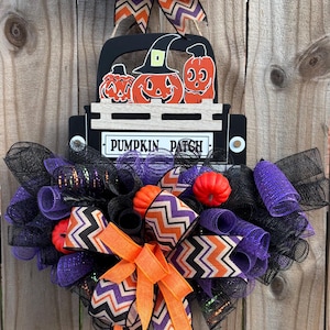 May include: A Halloween-themed wreath with a black truck carrying pumpkin cutouts. The wreath features black and purple mesh, orange and chevron patterned ribbons, and the text "PUMPKIN PATCH".
