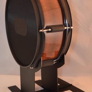 Peut inclure: Un tambour marron et noir avec un corps en bois et des peaux noires. Le tambour est monté sur un support en métal noir. Le tambour a une finition polie et est conçu pour les performances musicales.