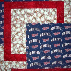 Puede incluir: Una colcha roja, blanca y azul con temática de béisbol. La colcha presenta un patrón de pelotas de béisbol y bates, así como las palabras "Minnesota Twins".