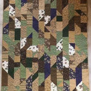 May include: A patchwork quilt with a geometric pattern in shades of brown, green, beige, and purple. The quilt is made of various fabrics with different patterns, including floral prints and stripes.