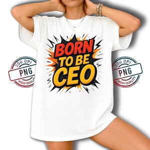 May include: White t-shirt with the text "BORN TO BE CEO" in a bold, colorful design. The graphic features red, orange, and yellow text with a black outline, set against a burst-like background. The shirt has short sleeves.